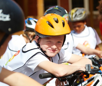 Child in a yellow cycling helmet, smiling at the camera.